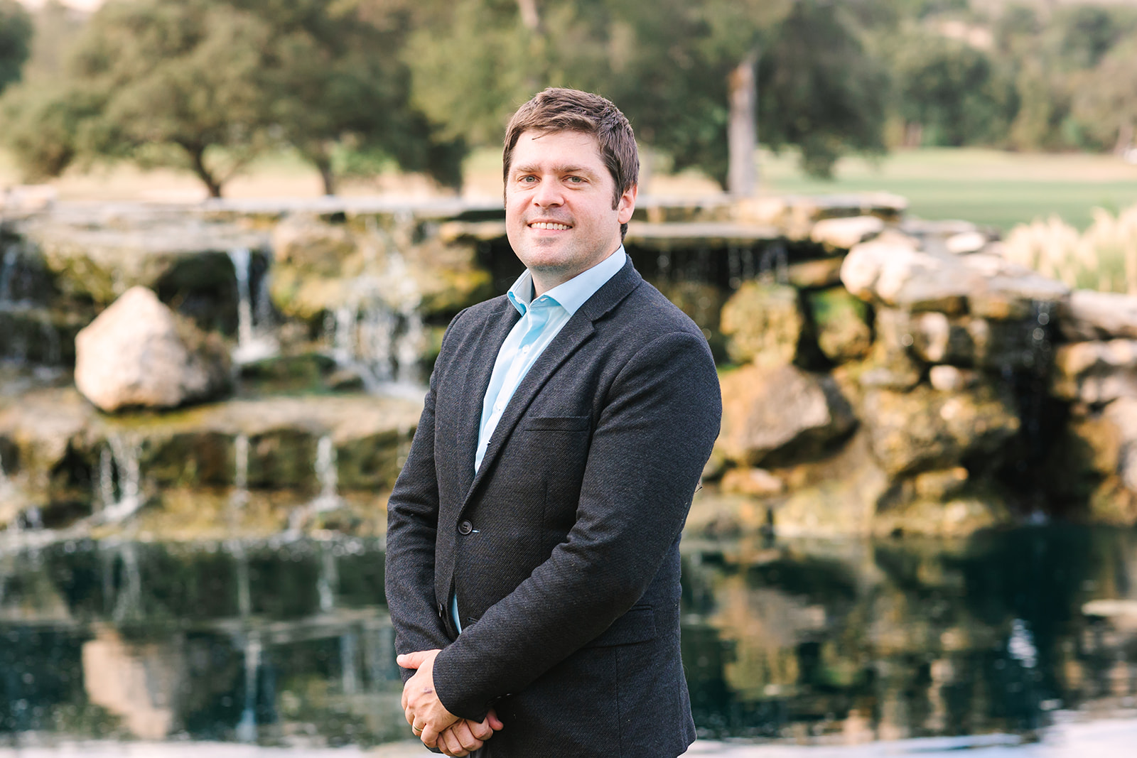 A man in a suit standing in front of a waterfall.